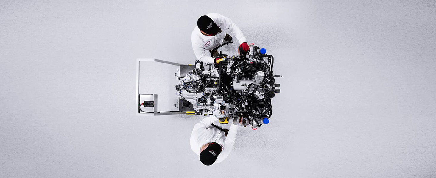 Overhead shot of two Acura engineers in whitespace, working on a futuristic engine.	Vue aérienne de deux ingénieurs Acura dans une salle blanche qui travaillent sur un moteur futuriste.