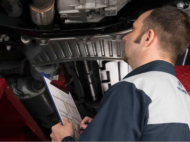 A certified Acura mechanic inspecting the under carriage of an Acura vehicle. // Un mécanicien Acura certifié inspectant le châssis d'un véhicule Acura